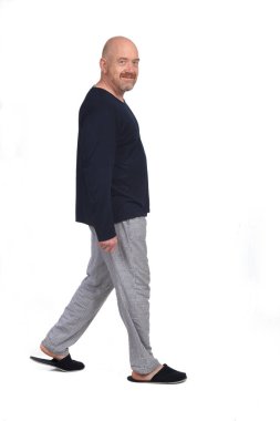 Beyaz arka planda yürüyen pijamalı bir adam kameraya bakıyor. 