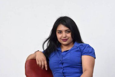 Latin Amerikalı kadın bir sandalyede oturmuş, rahatlamış ve kameraya bakıyor. 