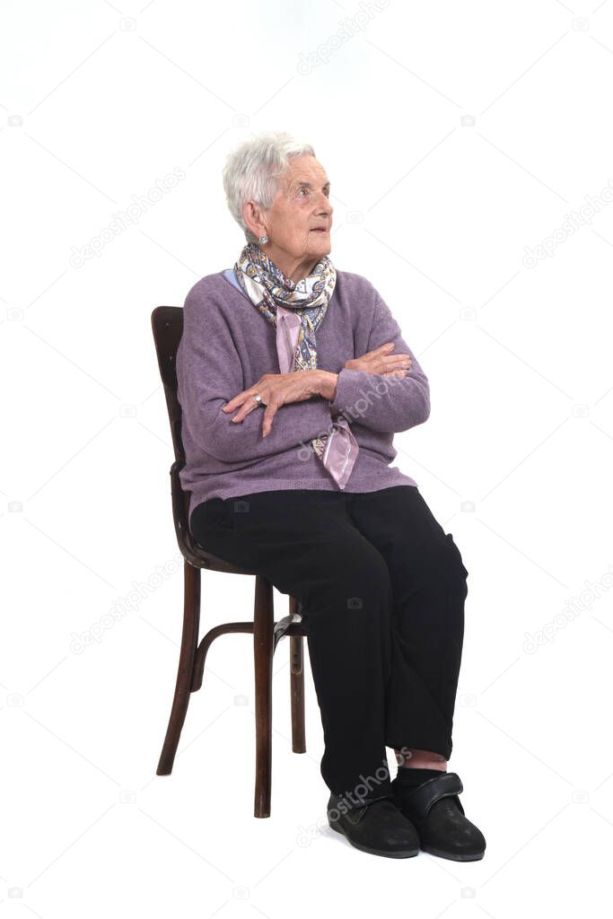 view of a senir woman sitting on chair looking up and arms crossed on white background