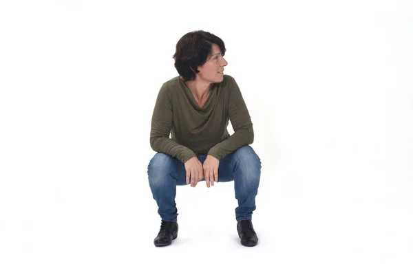 スクワットに座って白い背景を見ている女性の正面図 — ストック写真