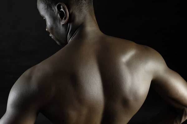 Back of a naked African boy, black background