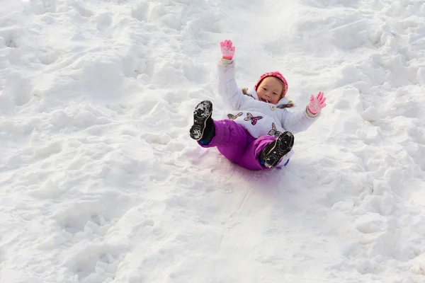 Het kleine meisje dia's zitten op een helling van ijs — Stockfoto