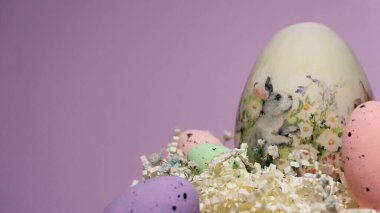 Renkli Paskalya yumurtaları süslü tavşan yumurtasıyla dekoratif yuvaya yerleştirilir. Turkuaz arka planda yumuşak pastel renklerle bahar Paskalya kompozisyonu.