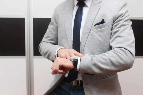 Stilig man i elegant grå kostym tittar på hans armbandsur Stockbild