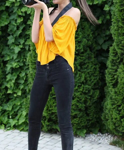 穿着黄色衬衫 蓝色牛仔裤和高跟鞋的模特正在拍照 那个女人拿着一台Dslr摄像头 — 图库照片