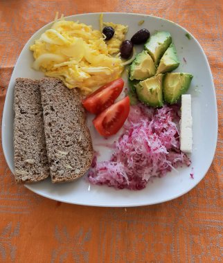 Kızarmış yumurta, avokado, beyaz tabakta servis edilen tam buğday ekmeği ve peynir.