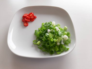 Beyaz tabakta doğranmış yeşil soğan ve kırmızı biber.