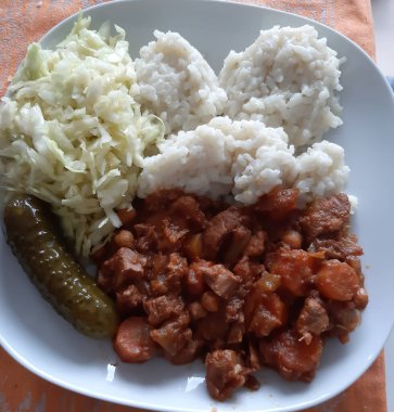 Tabakta lahana salatalı pilav, salatalık turşusu ve tavuk eti var.