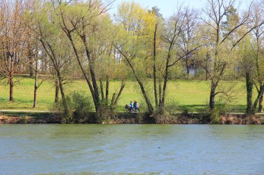 Regenburg, Almanya, 16 Nisan 2022: İnsanlar güzel Regensburg ilkbahar doğasında göl kenarındaki manzaralı kırsal bir yolda yürüyüp dinleniyorlar