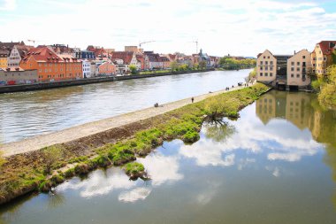 Regenburg, Almanya, 18 Nisan 2022: İlkbaharda Tuna Nehri kıyısındaki manzaralı caddede yürüyen insanlarla birlikte şehir manzarası