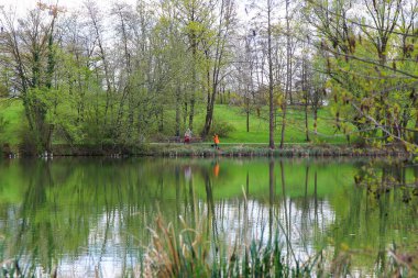 Regenburg, Almanya, 18 Nisan 2022: İnsanlar güzel Regensburg ilkbahar doğasında göl kenarındaki manzaralı kırsal bir yolda yürüyüp dinleniyorlar