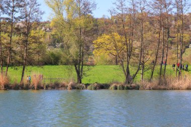 Regenburg, Almanya, 16 Nisan 2022: İnsanlar güzel Regensburg ilkbahar doğasında göl kenarındaki manzaralı kırsal bir yolda yürüyüp dinleniyorlar