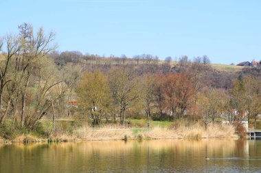 Regenburg, Almanya, 27 Mart 2022: İnsanlar güzel Regensburg ilkbahar doğasında göl kenarındaki manzaralı kırsal bir yolda yürüyüp dinleniyorlar