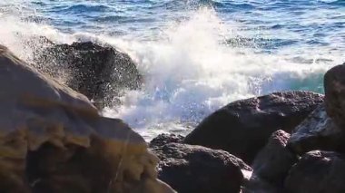 Yumuşak okyanus dalgaları, kışın açık mavi bir sahil köyünde kayaların üzerinde yuvarlanır.