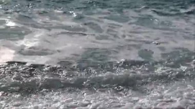 Yumuşak okyanus dalgaları, kışın açık mavi bir sahil köyünde kayaların üzerinde yuvarlanır.