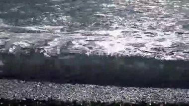 Yumuşak okyanus dalgaları, kışın açık mavi bir sahil köyünde kayaların üzerinde yuvarlanır.