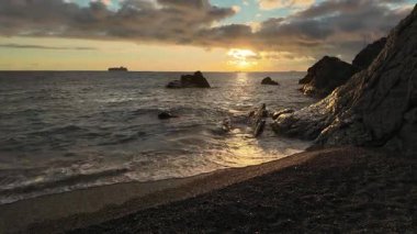 Bogliasco İtalya 'sındaki kara bulutların altında kumlu kayaları yıkayan sakin okyanus dalgaları üzerinde dramatik bir gün batımı..