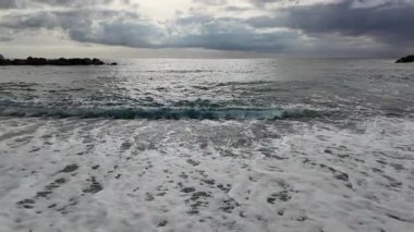 Yumuşak dalgalar, kışın sahil köyü Bogliasco 'da kumlu plajlara ağır çekim 120 fps hızla akıyor.