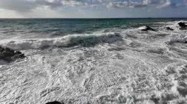 Güçlü okyanus dalgaları, Bogliasco İtalya 'da yavaş çekim 120 fps' de bulutlu gökyüzünün altında beyaz köpük oluşturan kayalık kıyılara vurur.