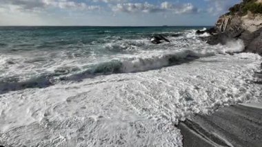 Güçlü okyanus dalgaları, Bogliasco İtalya 'da yavaş çekim 120 fps' de bulutlu gökyüzünün altında beyaz köpük oluşturan kayalık kıyılara vurur.
