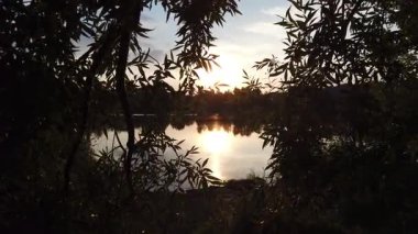 Altın güneş, Regensburg yakınlarındaki sakin göl suyuna yansıyan orman siluetlerinin ardında batıyor.