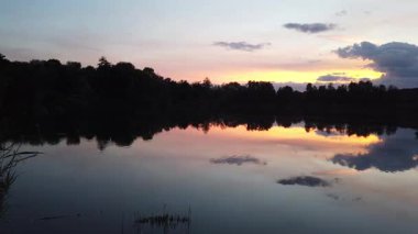 Altın güneş, Regensburg yakınlarındaki sakin göl suyuna yansıyan orman siluetlerinin ardında batıyor.