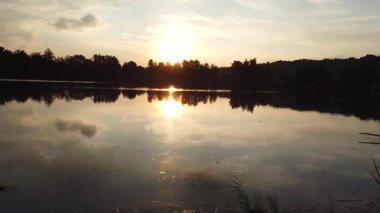 Altın güneş, Regensburg yakınlarındaki sakin göl suyuna yansıyan orman siluetlerinin ardında batıyor.