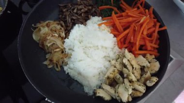 Geleneksel Kore bibimbap yemeği pişirirken renkli sebze ve pirinci bir tavada karıştırmak