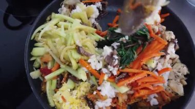 Geleneksel Kore bibimbap yemeği pişirirken renkli sebze ve pirinci bir tavada karıştırmak