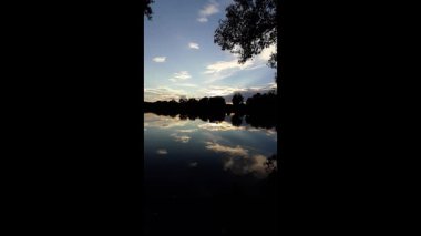 Altın güneş, Regensburg yakınlarındaki sakin göl suyuna yansıyan orman siluetlerinin ardında batıyor.