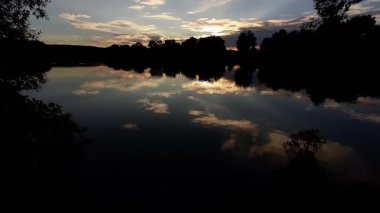 Altın güneş, Regensburg yakınlarındaki sakin göl suyuna yansıyan orman siluetlerinin ardında batıyor.