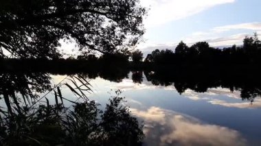 Altın güneş, Regensburg yakınlarındaki sakin göl suyuna yansıyan orman siluetlerinin ardında batıyor.