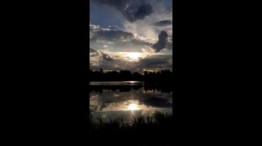 Altın güneş, Regensburg yakınlarındaki sakin göl suyuna yansıyan orman siluetlerinin ardında batıyor.