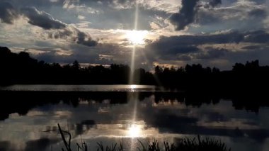 Altın güneş, Regensburg yakınlarındaki sakin göl suyuna yansıyan orman siluetlerinin ardında batıyor.