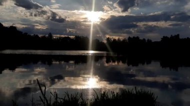Altın güneş, Regensburg yakınlarındaki sakin göl suyuna yansıyan orman siluetlerinin ardında batıyor.
