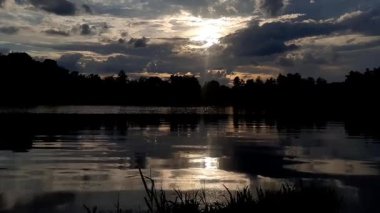 Altın güneş, Regensburg yakınlarındaki sakin göl suyuna yansıyan orman siluetlerinin ardında batıyor.