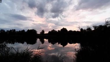 Altın güneş, Regensburg yakınlarındaki sakin göl suyuna yansıyan orman siluetlerinin ardında batıyor.