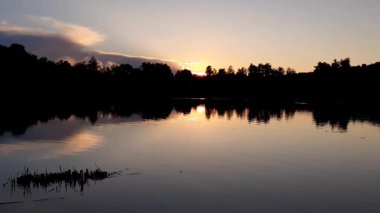 Altın güneş, Regensburg yakınlarındaki sakin göl suyuna yansıyan orman siluetlerinin ardında batıyor.