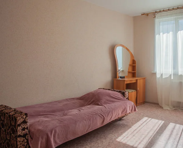 一张铺着毛毯的旧沙发 一个有镜子的支架 立在一间明亮房间的窗前 — 图库照片