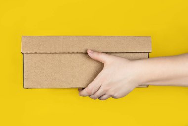 Sarı arka planda büyük bir karton kutu var. Yatay fotoğraf. Konsept - evinize kurye ile sipariş teslimatı, paket makbuzu, güvenli mesafe