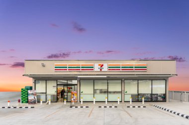 Bangkok, Tayland - 9 Aralık 2025: Günbatımı gökyüzü arka planına karşı aydınlatılmış ışıklandırma ve müşteri park alanı ile Büyük 7 Eleven Convenience Building Store.