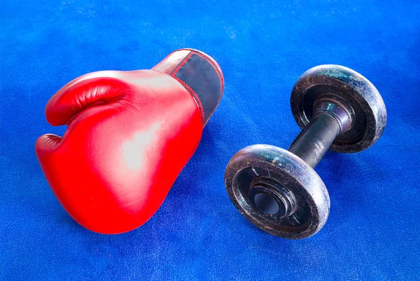 Luva de boxe vermelha e halteres velhos isolados em tapete de exercício azul — Fotografia de Stock