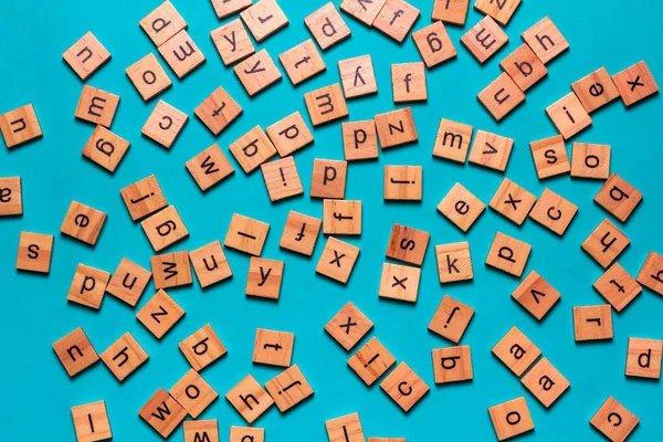 Kare ahşap karolardan yapılmış İngiliz alfabesi mavi arkaplana saçılmış. Düşünce geliştirme konsepti, dil bilgisi.