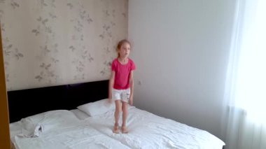 Mutlu bir kız beyaz çarşaflarla yatağa atlar ve kollarını sallar. Çal, eğlen, eğlen.