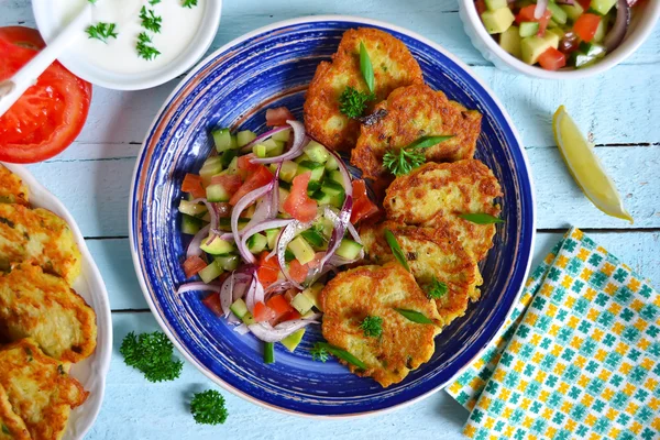 Crêpes de pommes de terre avec salade de légumes sur fond bleu — Photo