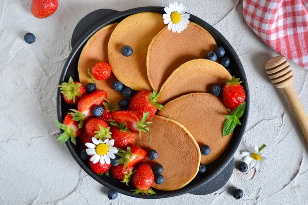 Pancakes with berries and honey in a pan on a concrete backgroun — Stock Photo, Image