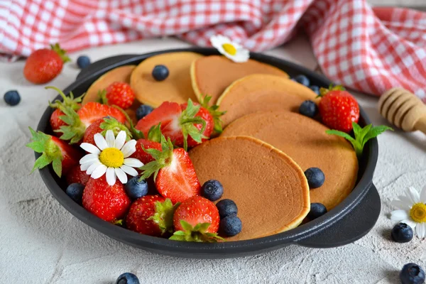 Pancakes with berries and honey in a pan on a concrete backgroun — Stock Photo, Image