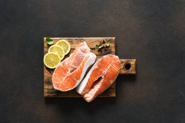 Baharatlı somon bifteği, ahşap bir tahtanın üzerinde, koyu beton bir arka planda pişirilmeye hazır..