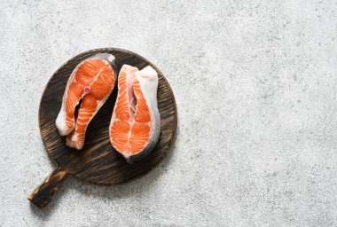 Baharatlı somon bifteği hafif beton arka planda yuvarlak ahşap bir tahtanın üzerinde pişirmeye hazır..