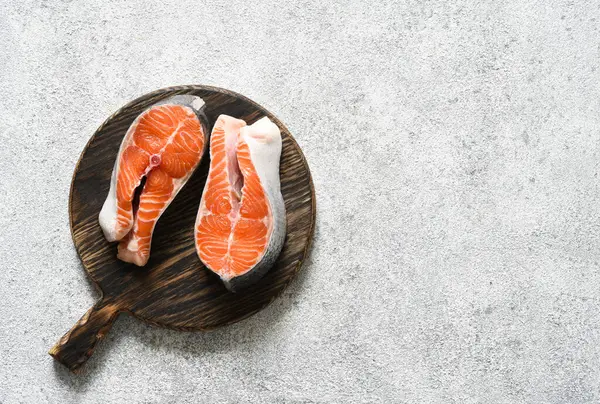 Baharatlı somon bifteği hafif beton arka planda yuvarlak ahşap bir tahtanın üzerinde pişirmeye hazır..